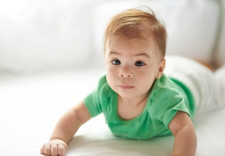 Worried baby girl laying on white bed backgroundの写真素材