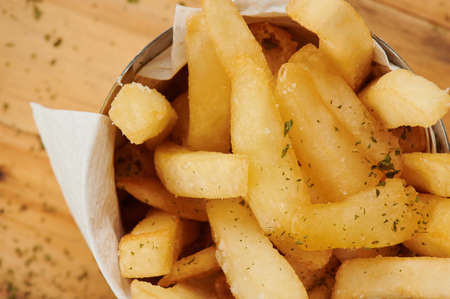 Crispy french fries in cup on wooden table close up viewの写真素材