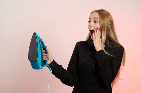 Screaming young girl with iron in hand isolated on pink background