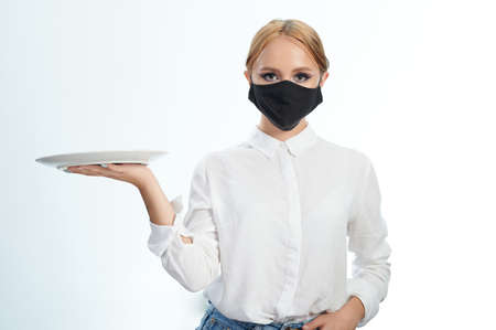 Waitress in mask with plate in hand on side isolated on white studio backgroundの写真素材