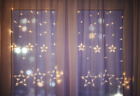Christmas decoration lights under window curtain on blurred street backgroundの写真素材