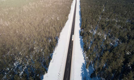 Cargo truck moving on highway road around snowy forest aerial above top viewの写真素材