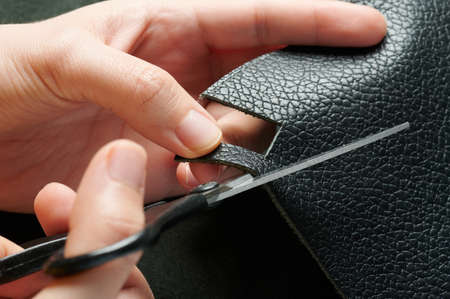 Craftman with scissors cut slice of black leather macro close up viewの写真素材