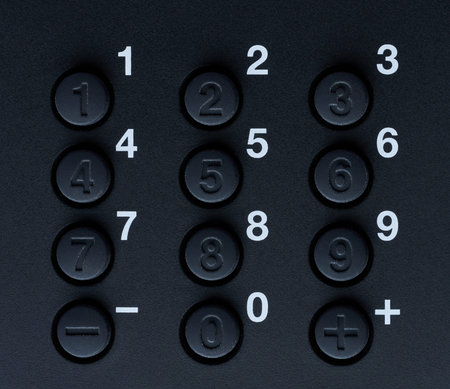 Black plastic keyboard with number buttons on dark surface close up view. Real plastic buttons