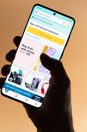 New york, USA - November 4, 2022: Using amazon shopping app on smartphone holding in hand isolated on brown backgroundのeditorial素材