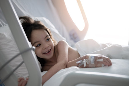 Happy kid girl in clink bed lay with iv in handの写真素材