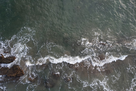 Curly wave splash at sea near stone rock coast aerial above top view
