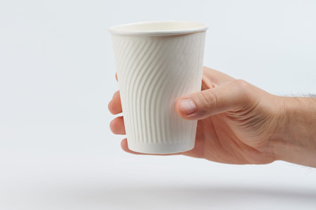 Clean white paper cup for drink in hand side view isolated