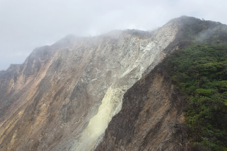 Volcano crater with yellow sulfur slope in smoke cloud skyの写真素材
