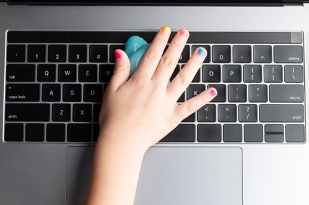 Hand with colorful nails remove dust from laptop keyboard above top viewの写真素材