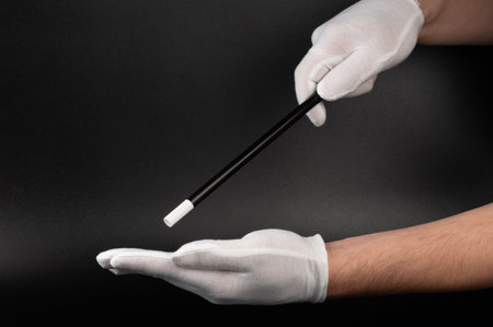 Hands in white glove with magical stick on black backgroundの写真素材