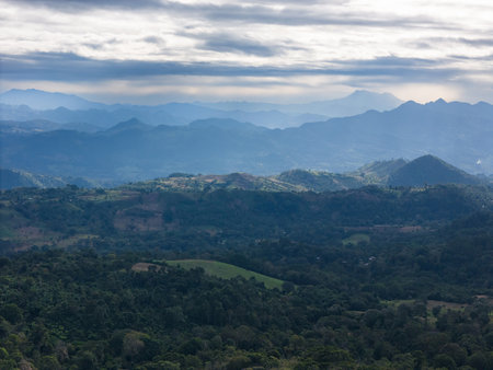Vast green hills and mountains blend into horizon under cloudy sky in early morning light, showcasing nature's beauty.の写真素材