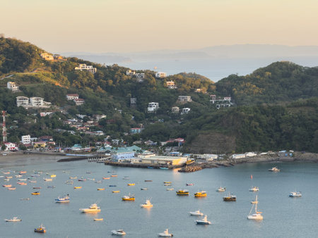 Tranquil harbor adorned with numerous boats rests near charming seaside town at sunset, showcasing stunning landscapes.の写真素材