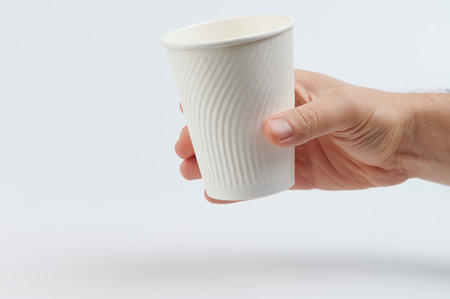 Blank white paper cup in hand side view isolated on studio backgroundの写真素材