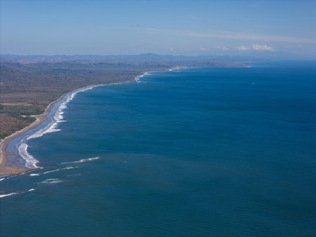 Waves crash gently on sandy beach, framed by cliffs and clear skies along vibrant coastline.の写真素材