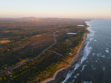 Breathtaking view of coastline at dusk, highlighting gentle ocean waves, greenery, and distant hills.の写真素材