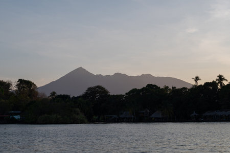 A tranquil lake reflects the silhouette of a majestic volcano as twilight casts soft hues over the landscape.の写真素材