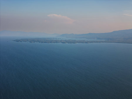 Soft hues blend above calm waters as dusk settles over distant hills and islands, creating peaceful atmosphere.の写真素材