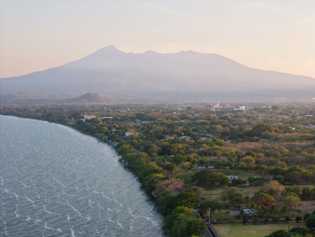 Calm waters reflect the soft light of dawn as mountains loom in the background, highlighting the lush landscape.の写真素材