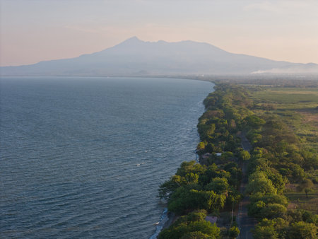 Stunning view of curved coastline lined with trees, overlooking calm sea and distant mountain at sunset.の写真素材