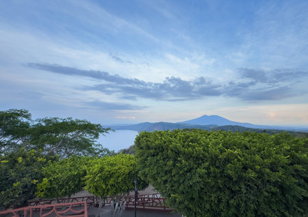 Wide view of calm lake surrounded by trees and distant mountains during sunset, creating peaceful atmosphere.の写真素材