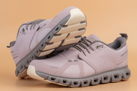 Modern gray athletic shoes positioned elegantly on neutral beige surface showcase their design and features.の写真素材
