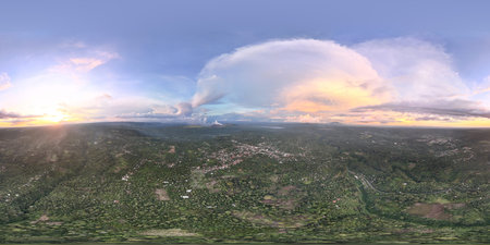 Sunset casts warm colors over green valley, mountains stand in distance, and clouds drift across...
