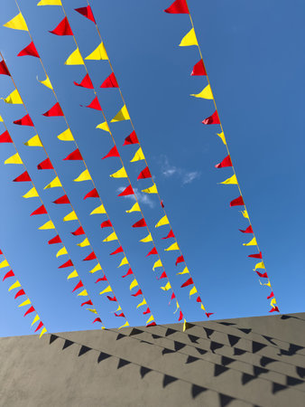 Bright red, yellow, and black flags hang above a sandy area, creating a festive atmosphere under a clear blue sky.の写真素材