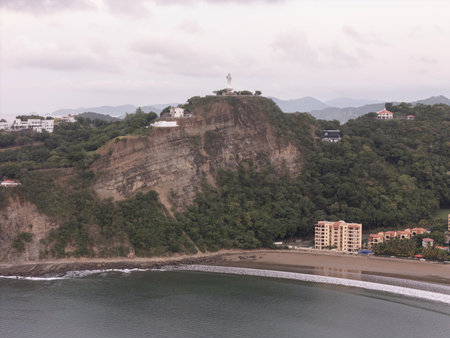 The scene shows a cliffside village overlooking the ocean, surrounded by lush trees under a cloudy sky.の写真素材