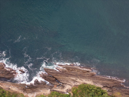 Ocean hit big rock in shoreline above top drone view with blue waterの写真素材