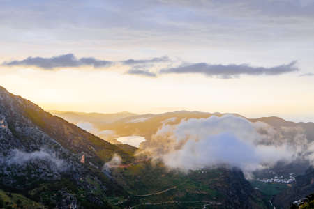 Picturesque mountain valley filled with curly clouds at sunset.の写真素材