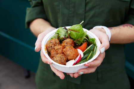 man holding a white bowl with greens, red radish and meatballs