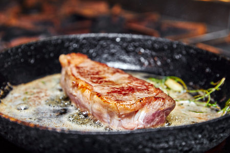 frying pan on a stove on which a large piece of meat is fried with butterの写真素材