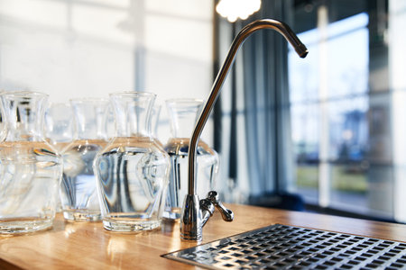 water tap next to many glass large vases standing on a wooden countertop, kitchen
