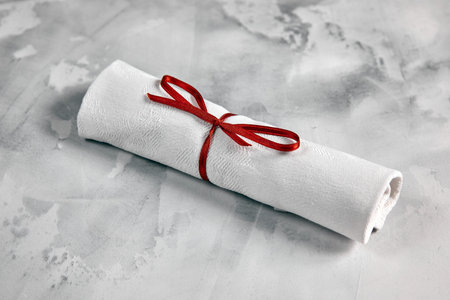 twisted napkin tied with a red bow, lies on a white marble background, decorationの写真素材