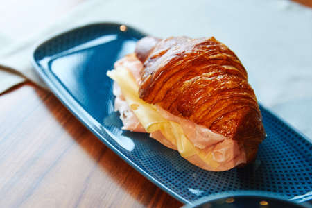 ham and cheese croissant, hot, lies on a blue plate, pastries, on a wooden tableの写真素材