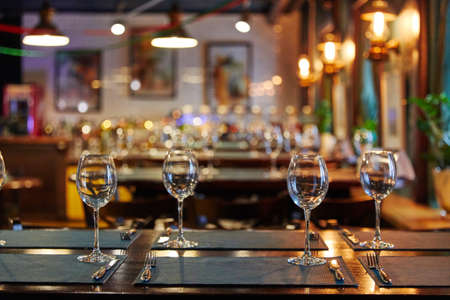 empty glass goblets glasses on a wooden table, next to forks, restaurantの写真素材