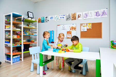 Russia, Moscow, 01.01.2019, two girls and a boy in kindergarten are sitting at a table and playing toysのeditorial素材