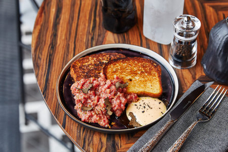 meat with fried loaf and sauce, lies on a plate, which stands on a wooden table next to spices and cutleryの写真素材
