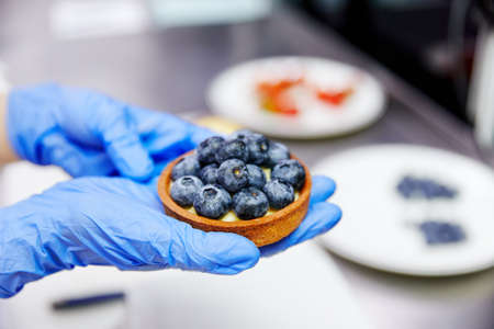 man holds in hands in blue gloves, in a bowl a blueberry, close-upの写真素材