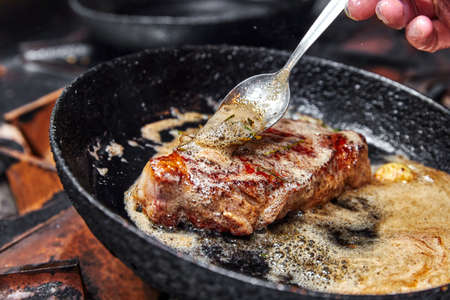 frying pan on a stove on which a large piece of meat is fried with butter, garlic and herbsの写真素材