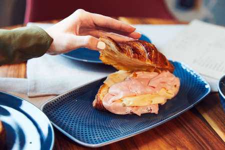 a puff pastry with ham cheese, cut in half, pour on a blue plate, a man looks with his hand the ingredients that are insideの写真素材