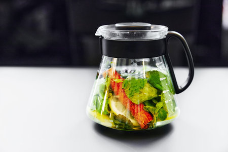 lemonade in a transparent teapot with mint and herbs on a white table