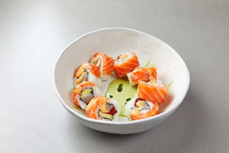 Sushi Uramaki with salmon, green algae, rolls poured with sauce wrapped in fish and, with spices, in a white bowlの写真素材