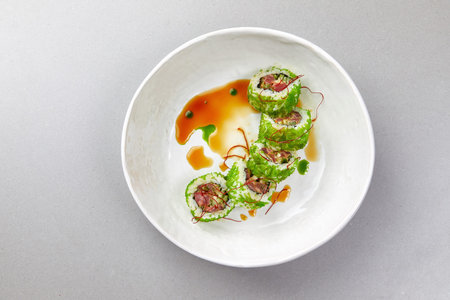 sushi uramaki with fish, green seaweed with sauce in a white bowl