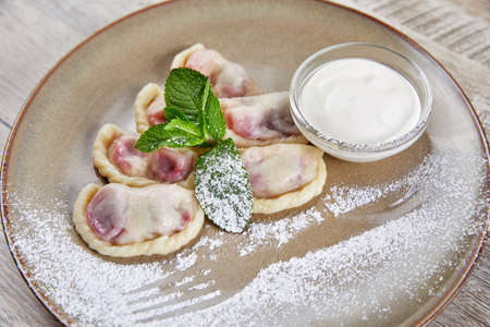 dumplings with berry filling, with sour cream laid out on plate decorated with mint leavesの写真素材