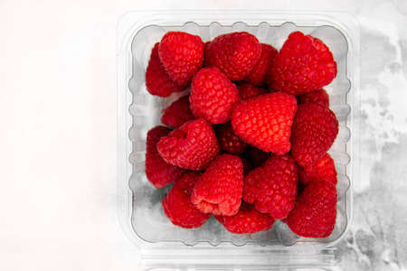 ripe raspberries lies in a plassmas box on a white backgroundの写真素材