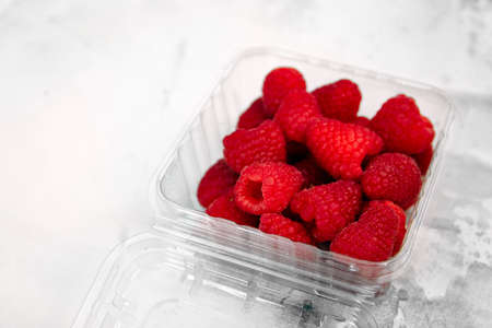ripe raspberries lies in a plassmas box on a white backgroundの写真素材