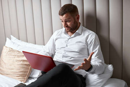 Surprised young businessman with laptop in bedの写真素材