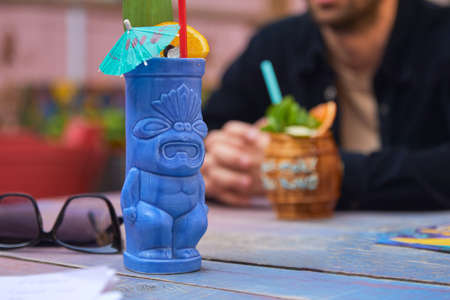 Tropical cocktail with orange in blue tiki style glass on wooden backgroundの写真素材